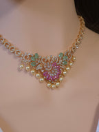 A gold-plated statement choker necklace with faux pearls, pink gemstone floral motifs, and green leaf accents, displayed on a mannequin bust.