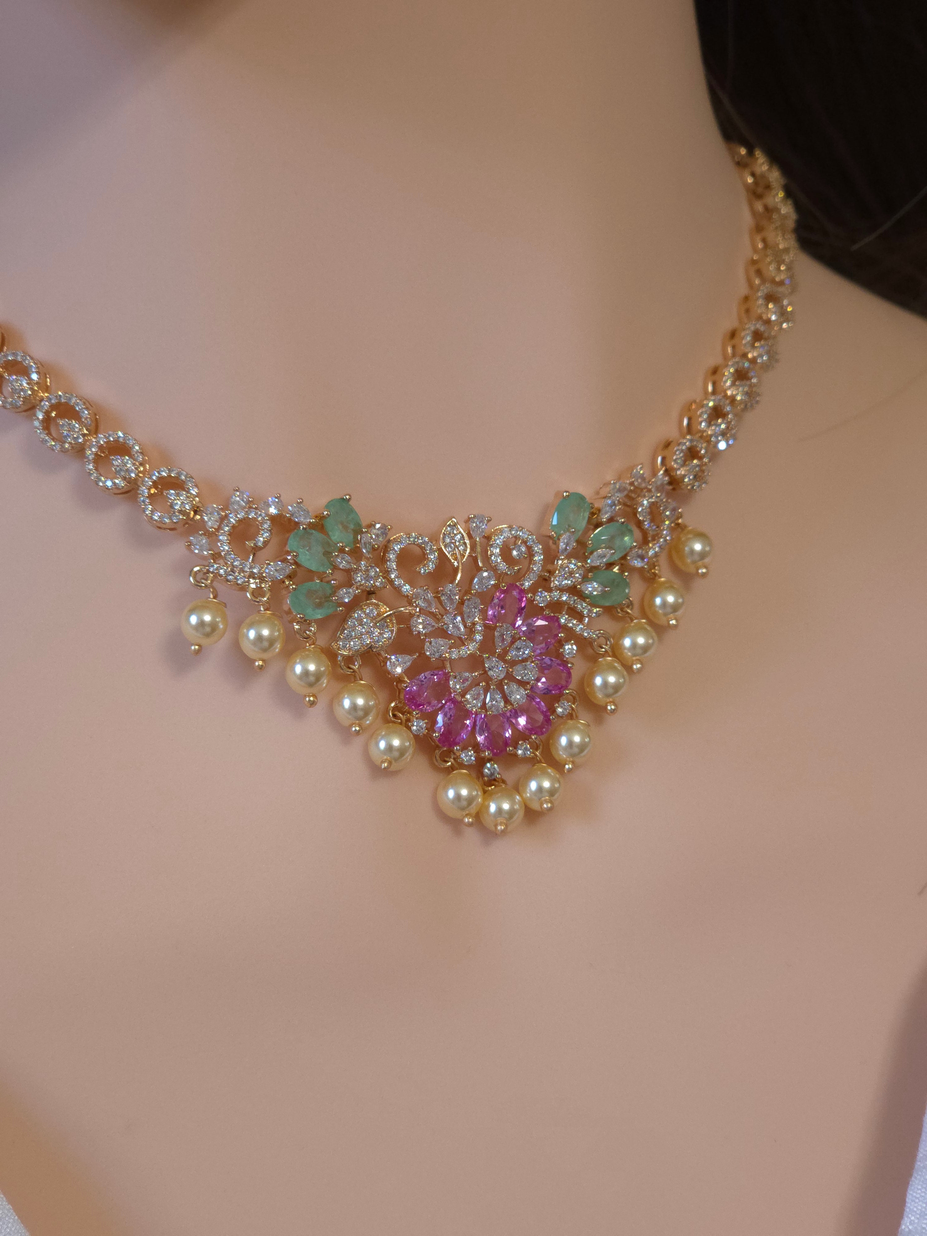 A gold-plated statement choker necklace with faux pearls, pink gemstone floral motifs, and green leaf accents, displayed on a mannequin bust.