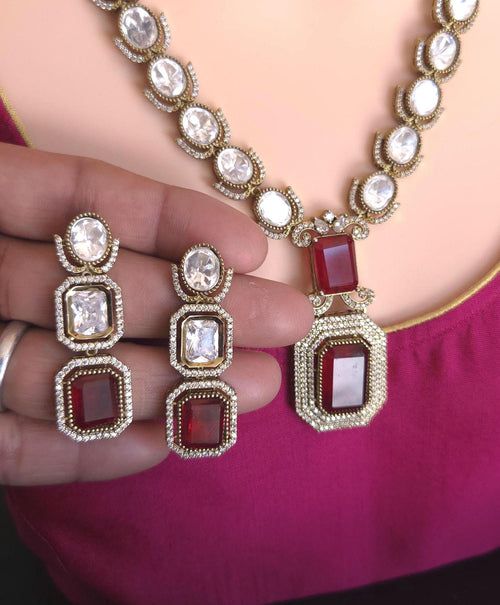 Necklace and earrings with red and clear gemstones held by a hand.