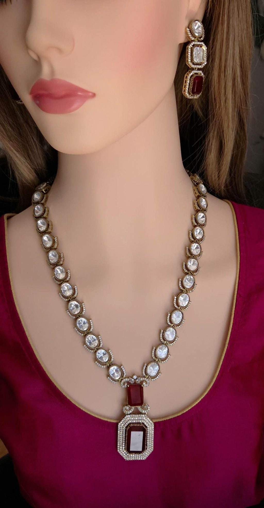 Mannequin wearing a decorative necklace and earrings with red and white stones.