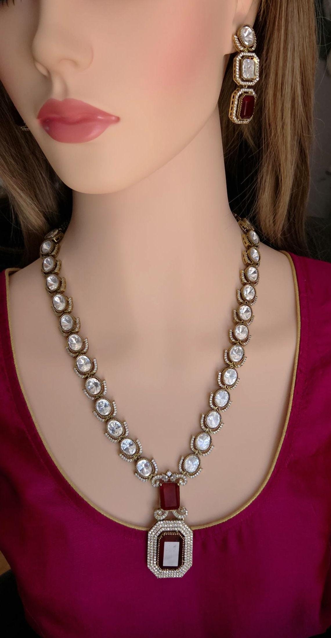 Mannequin wearing a decorative necklace and earrings with red and white stones.