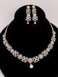 Gold and silver-tone jewelry set featuring a necklace and matching earrings displayed on a black velvet bust. The necklace has repeating geometric and floral motifs with a teardrop pendant, and the matching earrings are shown above the bust against a light gray background.