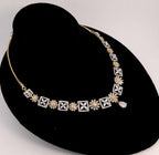 A gold and white diamond necklace displayed on a black velvet jewelry bust against a light gray background.