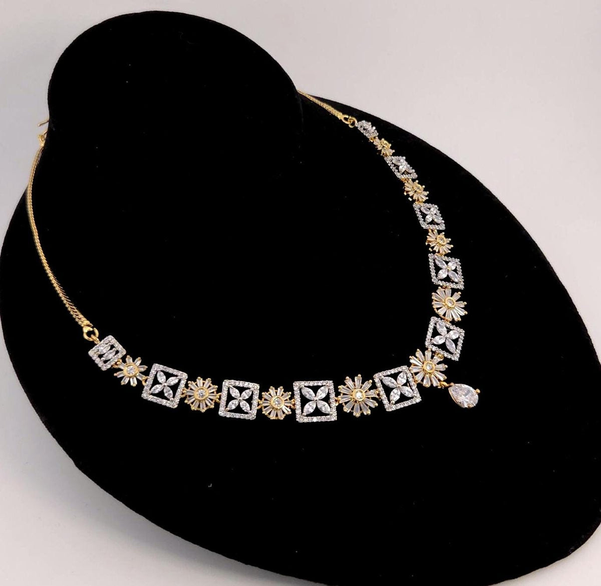 A gold and white diamond necklace displayed on a black velvet jewelry bust against a light gray background.