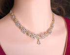 A gold and silver-toned diamond necklace with floral and geometric motifs, displayed on a mannequin bust wearing a maroon top.
