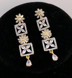 A pair of gold and crystal drop earrings displayed on a black velvet jewelry stand. The earrings feature floral and geometric patterns with clear crystals.