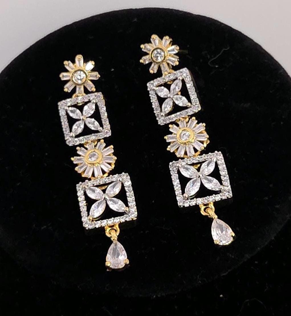 A pair of gold and crystal drop earrings displayed on a black velvet jewelry stand. The earrings feature floral and geometric patterns with clear crystals.