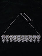 A silver-toned choker necklace with rectangular clear stones and ornate dangling filigree details, displayed against a black fabric background.