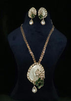 Gold-tone necklace and matching drop earrings displayed on a black velvet jewelry bust. The necklace features a large oval pendant with a white cameo-style face, surrounded by clear rhinestones and a green leaf motif, with a teardrop crystal drop below.