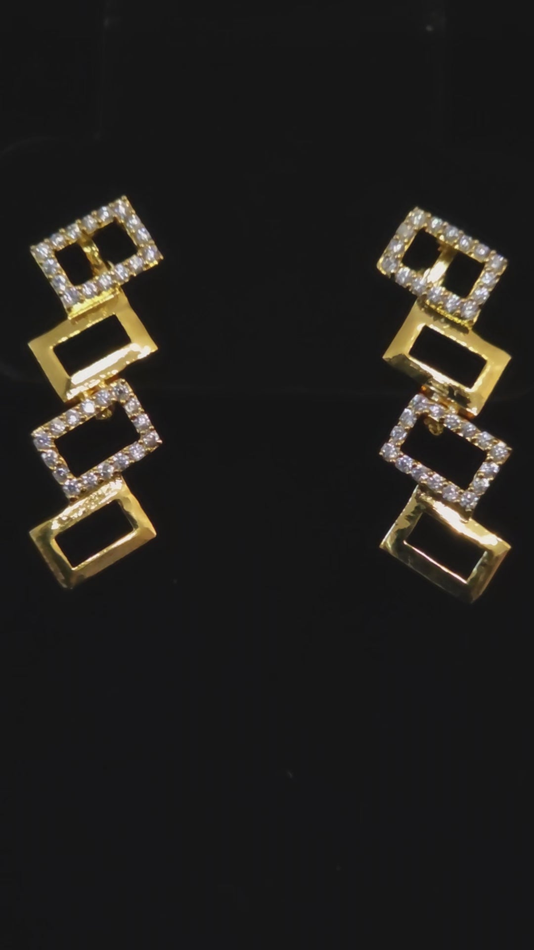 video of A gold and silver geometric jewelry set featuring a necklace and matching drop earrings, displayed on a black background.
