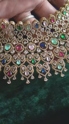 Navratan CZ Filigree Bib Choker, Chandelier Earring & Maang Tikka Bridal Set Zarkash – wide multicolor CZ filigree bib choker with emerald, ruby, sapphire, pink & white CZ stones, matching long chandelier earrings, and open-work heart maang tikka in gold finish