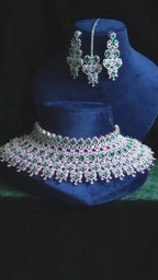 Emerald CZ Bib Choker, Chandelier Earring & Maang Tikka Bridal Set Noorjahan – wide multi-row oval emerald CZ bib choker with heart-arch teardrop fringe, long geometric chandelier earrings, and open-work heart maang tikka in silver finish