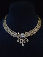 A gold-toned statement necklace with clear teardrop and oval gemstones, displayed on a black velvet jewelry bust.