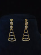 A pair of gold drop earrings with clear gemstones, displayed on a black velvet jewelry stand.