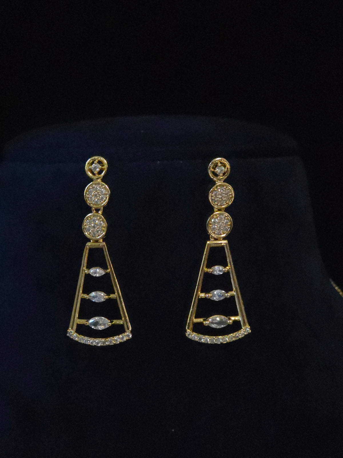A pair of gold drop earrings with clear gemstones, displayed on a black velvet jewelry stand.