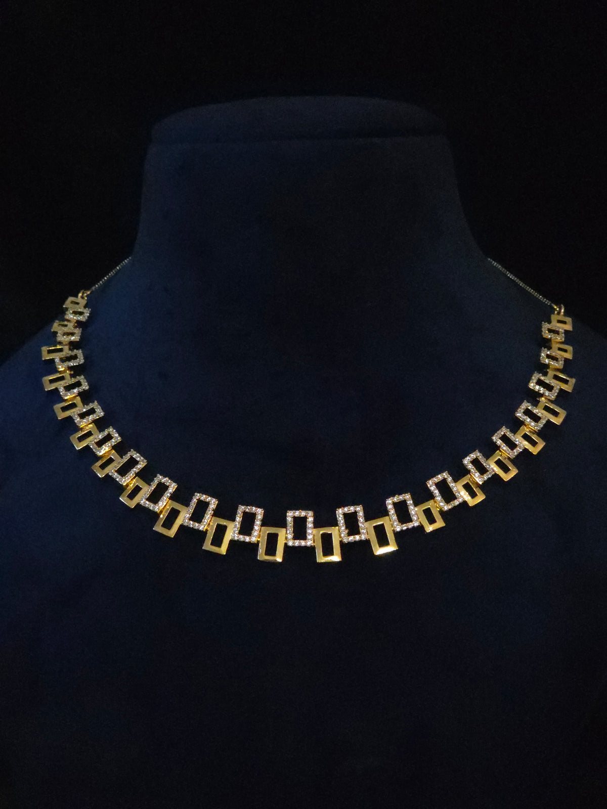 A gold and silver geometric jewelry set featuring a necklace and matching drop earrings, displayed on a black background.