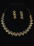 A gold and silver geometric jewelry set featuring a necklace and matching drop earrings, displayed on a black background.