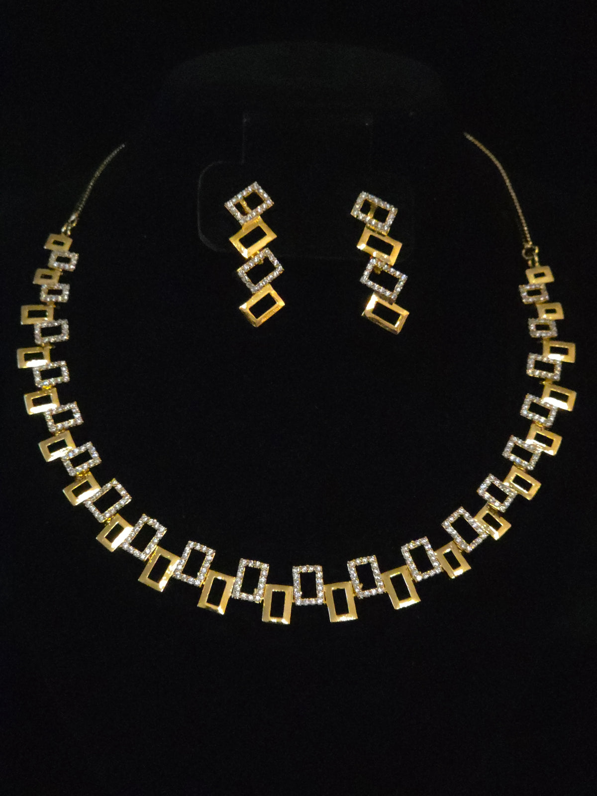 A gold and silver geometric jewelry set featuring a necklace and matching drop earrings, displayed on a black background.