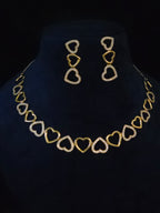 Gold heart link necklace and matching drop earrings displayed on a black velvet jewelry bust. The necklace and earrings feature alternating solid gold and open heart designs, with the open hearts embellished with small clear stones.