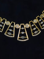 Gold geometric statement necklace with clear marquise and round gemstones, displayed on a black background.