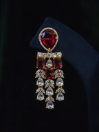 Close-up of a gold-plated ruby CZ chandelier earring with rectangular red stones and layered clear CZ tassels