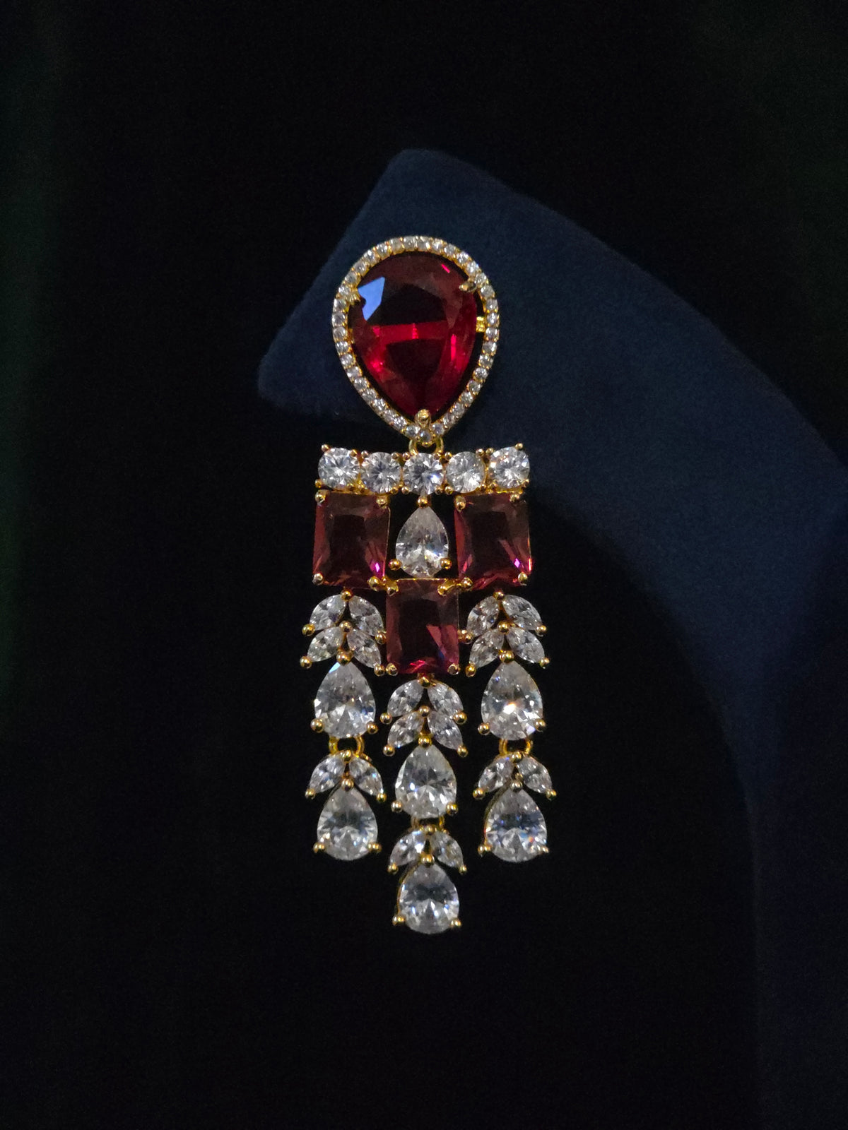 Close-up of a gold-plated ruby CZ chandelier earring with rectangular red stones and layered clear CZ tassels