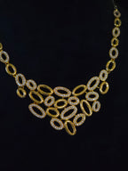A gold statement necklace with a bib-style arrangement of oval links, some encrusted with clear rhinestones, displayed on a black mannequin bust.