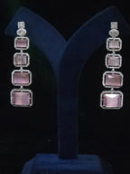 A pair of long drop earrings with four rectangular pink stones in silver settings, displayed on a dark blue velvet jewelry stand 
