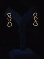 A pair of gold heart drop earrings with small clear stones, displayed on a black velvet jewelry stand against a black background.