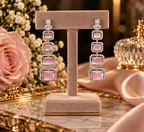 A pair of long drop earrings displayed on a beige jewelry stand. The earrings feature rectangular pink gemstones surrounded by clear crystals, set in a yellow-gold-toned metal.