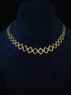 A gold geometric diamond-link chain necklace displayed on a black velvet jewelry bust.