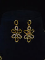A pair of gold-toned dangle earrings with openwork floral or butterfly-like cutouts, each adorned with small clear stones, displayed on a black velvet jewelry bust.