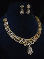 Gold-toned traditional jewelry set featuring an ornate choker necklace with a teardrop pendant and matching drop earrings, displayed on a black velvet jewelry bust.