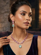 A woman wearing a pink gemstone necklace with a mint green pendant and matching drop earrings, styled with a dark purple velvet dress in a dimly lit interior setting.