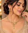 Model showcasing Gold-toned traditional Indian jewelry set featuring a necklace and matching earrings with intricate beadwork, floral motifs, and clear stone accents, 