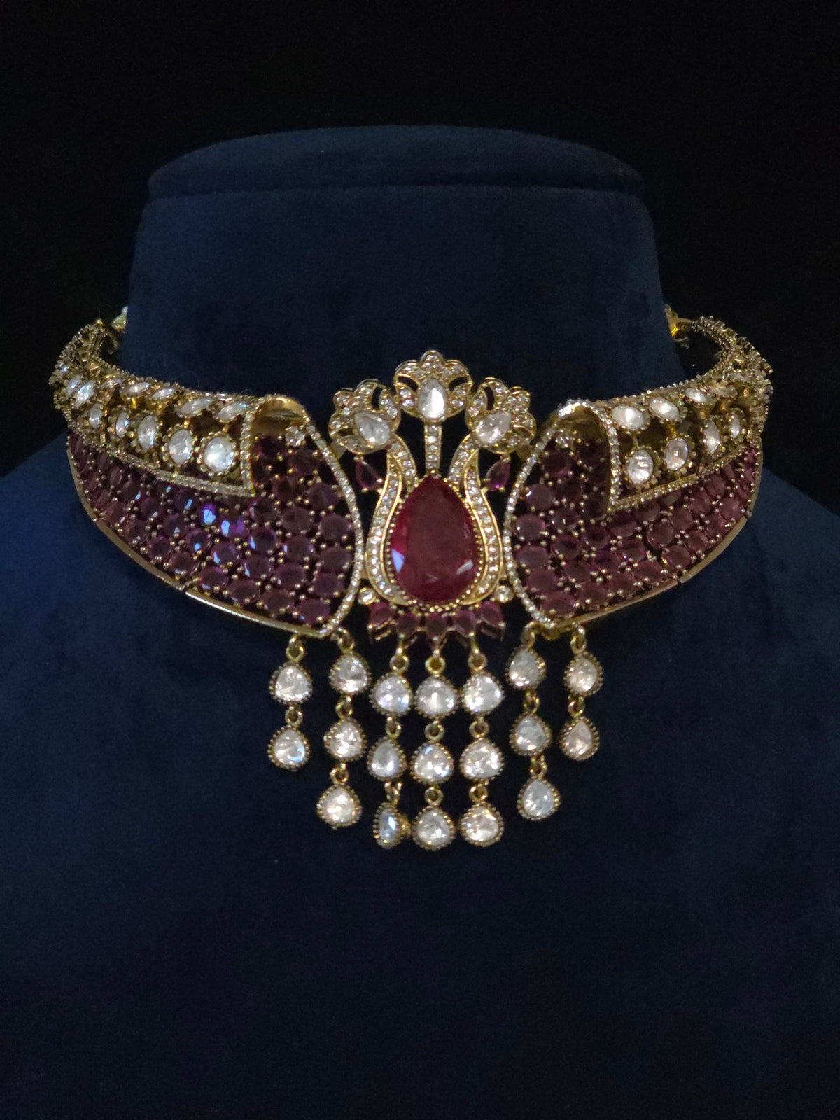 Front view of the broad bridal choker with wine-red stones, clear accents, and a teardrop center on a dark display bust.