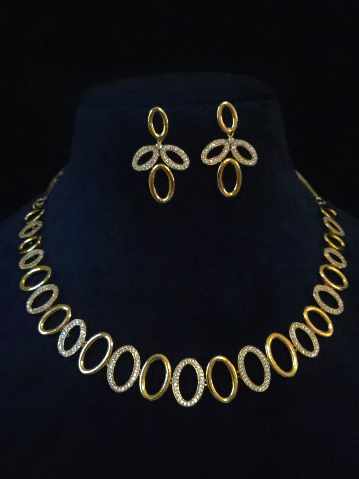 Gold-tone jewelry set featuring a matching necklace and earrings with oval links, displayed on a black velvet mannequin bust.