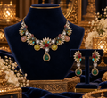 Multicolor gemstone leaf necklace and matching drop earrings with emerald pendant displayed on a navy velvet jewelry bust