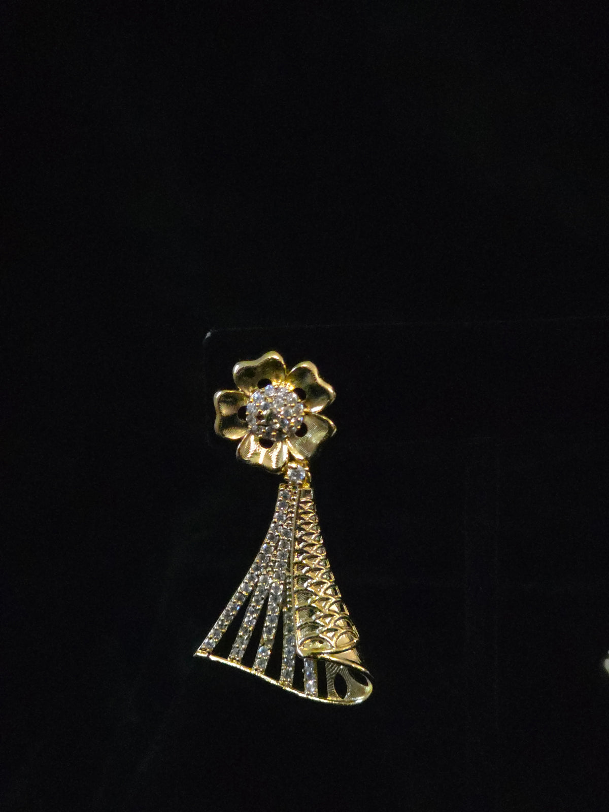 A gold-tone flower-shaped brooch with a dangling tassel design, embellished with clear rhinestones, displayed on a black background.