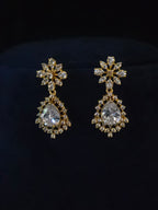 A pair of gold-toned drop earrings with clear teardrop-shaped crystals and surrounding clear stones, displayed on a black velvet surface.
