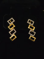 A pair of gold geometric drop earrings with rectangular links, some bordered in clear stones, displayed on a black background.