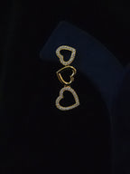 A gold-toned heart-shaped brooch or pin with pavé-set clear stones, displayed on a dark navy jewelry bust against a black background.