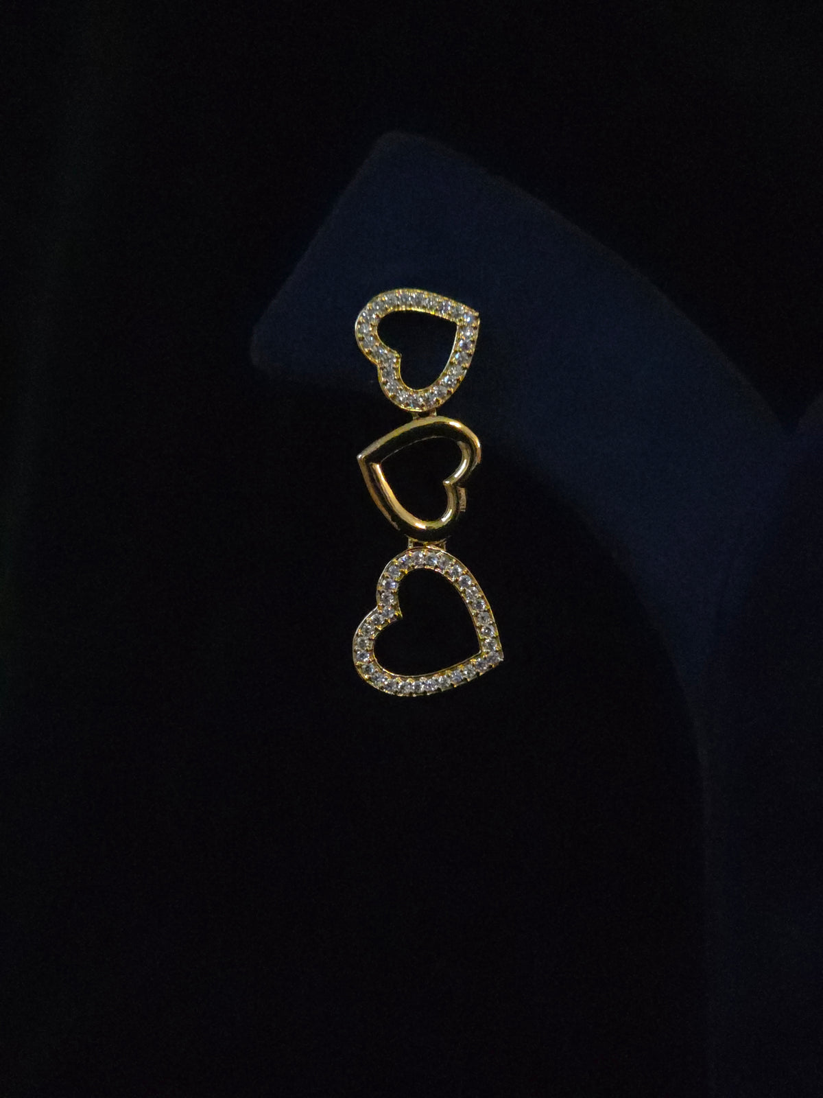 A gold-toned heart-shaped brooch or pin with pavé-set clear stones, displayed on a dark navy jewelry bust against a black background.