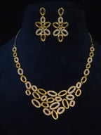 Gold-tone jewelry set featuring a statement collar necklace and matching drop earrings, both adorned with clear rhinestones, displayed on a black velvet bust.