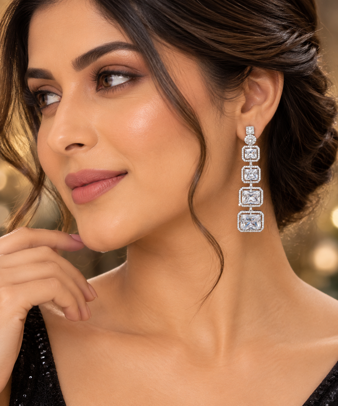 A close-up lifestyle shot of a woman wearing a long, multi-stone drop earring with square-cut clear stones in a silver-toned setting. The background is a soft, warm, blurred bokeh.