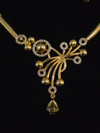 A gold-toned traditional necklace featuring a decorative floral and geometric pendant with small clear stones, set against a solid black background.