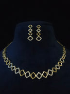 Gold geometric necklace and matching drop earrings displayed on a dark blue velvet jewelry bust against a black background.