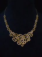 A gold statement necklace with a bib-style arrangement of oval links, some encrusted with clear rhinestones, displayed on a black mannequin bust.