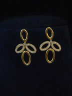 A pair of gold-tone drop earrings with oval and looped cutout details, set with small clear stones, displayed on a dark navy velvet jewelry stand.