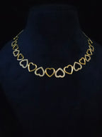 A gold heart-link necklace displayed on a black velvet jewelry bust against a black background.